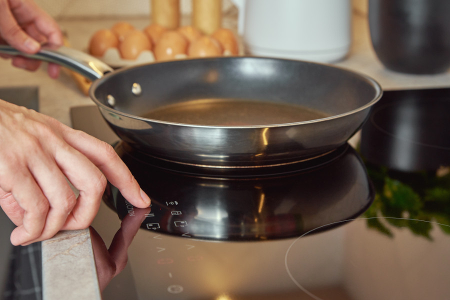 En person sätter en stekpanna på en spis och sätter på värmen